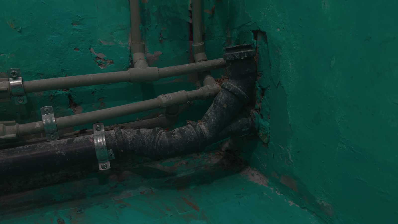 Exposed supply lines and a corroded cast-iron drain pipe on an interior wall