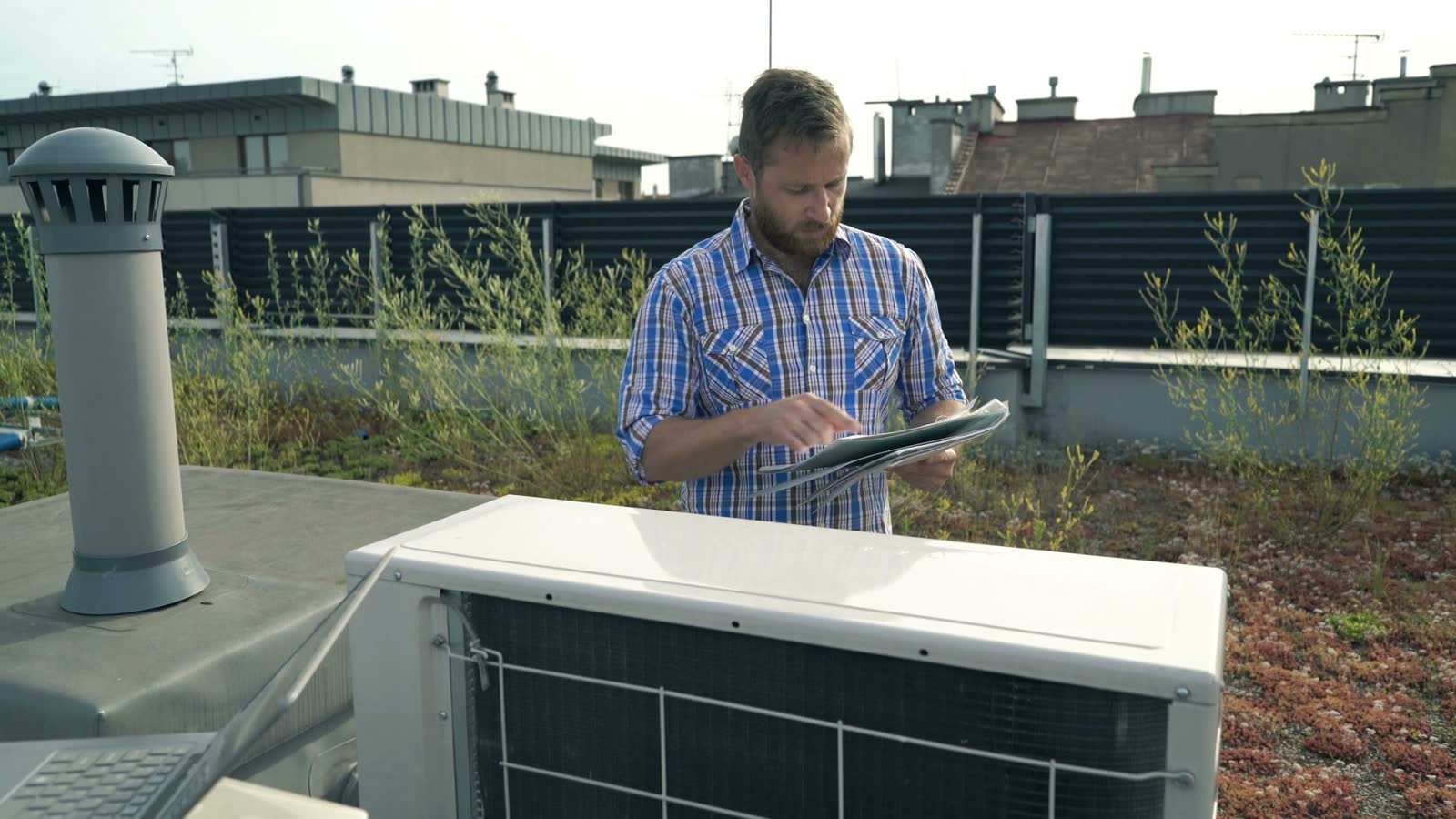 man-inspecting-hvac-system-with-laptop-on-rooftop.mp4